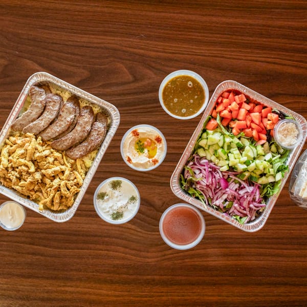 Zest Mediterranean Cuisine catering spread with meat, rice, salad, hummus, and sauces on a wooden table.