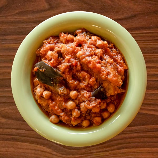 A light green bowl filled with Zest Mediterranean Cuisine's chickpea and eggplant stew in tomato sauce.
